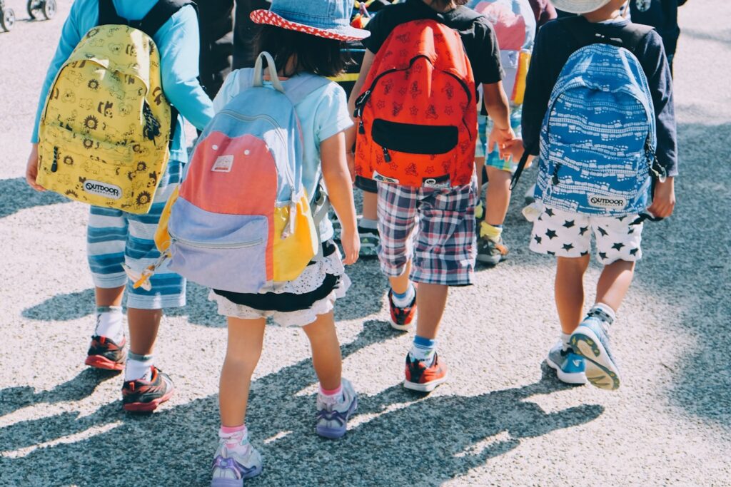 group of people wearing white and orange backpacks walking on gray concrete pavement during daytime