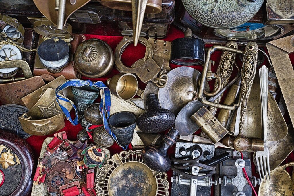 Diverse Collection of Vintage Antiques and Artifacts Displayed at a Local Market - A vibrant assortment of vintage antiques and artifacts is laid out on a market table, showcasing various items including clocks, lock mechanisms, and decorative trinkets. Shoppers explore the unique pieces, each with its own story, while traders engage in lively discussions about the history and craftsmanship behind these collectibles.