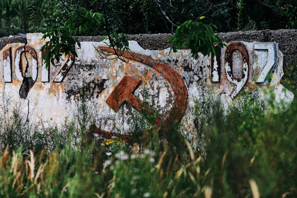Destroyed wall of a building from Russia with the number (year) 1917, sickle and hammer. Vintage soviet-era building falling apart in modern Russia. Grunge symbol of the revolution in cracks among the grass and desolation in the countryside